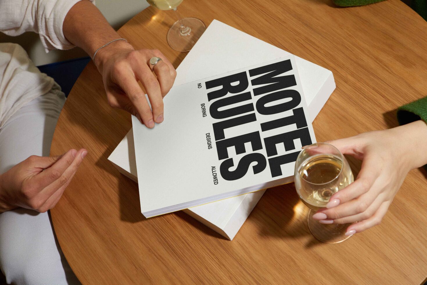 Designers discussing a book titled Motel Rules on wooden table with wine glasses. Concept for design inspiration, typography, graphic mockup, modern aesthetics.