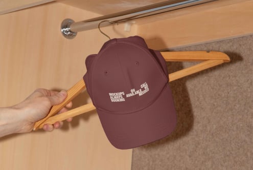 A burgundy cap on a wooden hanger with text detailing mockup availability. Ideal for designers seeking mockup resources. Keywords: mockup, cap, design.