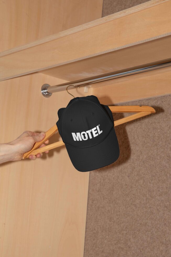 Black cap with Motel text on a wooden hanger in a closet mockup. Ideal for showcasing apparel designs. Fashion, branding, presentation asset.