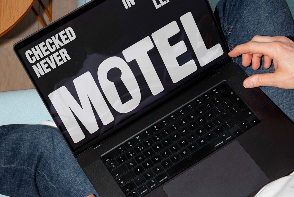 Dark laptop screen showing bold white motel typography with checked never