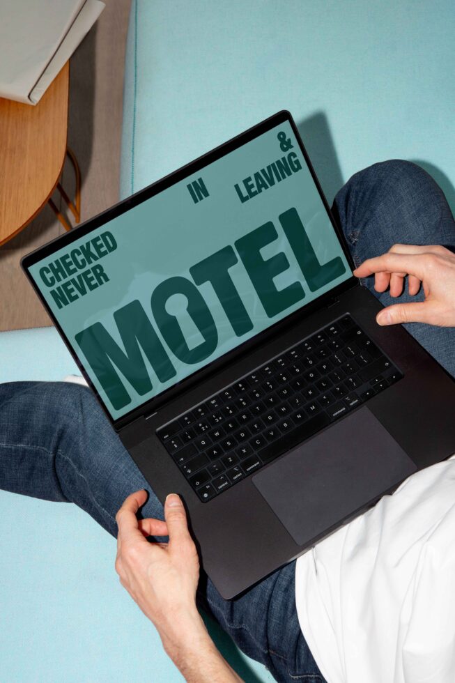 Man using a black laptop on light blue sofa displaying bold font graphic saying Motel Never Checked In Leaving suitable for font mockup templates.