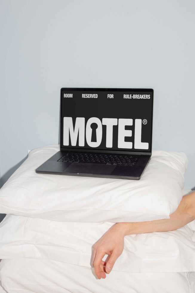 Laptop on pillows displaying Motel graphic with text Room Reserved for Rule-Breakers. Conceptual mockup for designers with creative workspace theme.