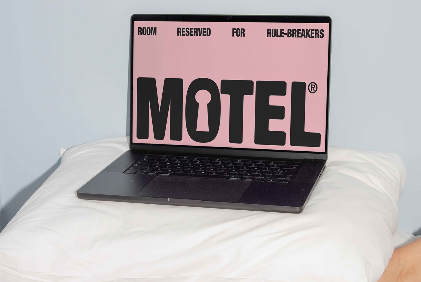 Laptop displaying pink graphic screen with bold text Motel with a keyhole on a pillow. Modern design mockup for showcasing digital branding assets.