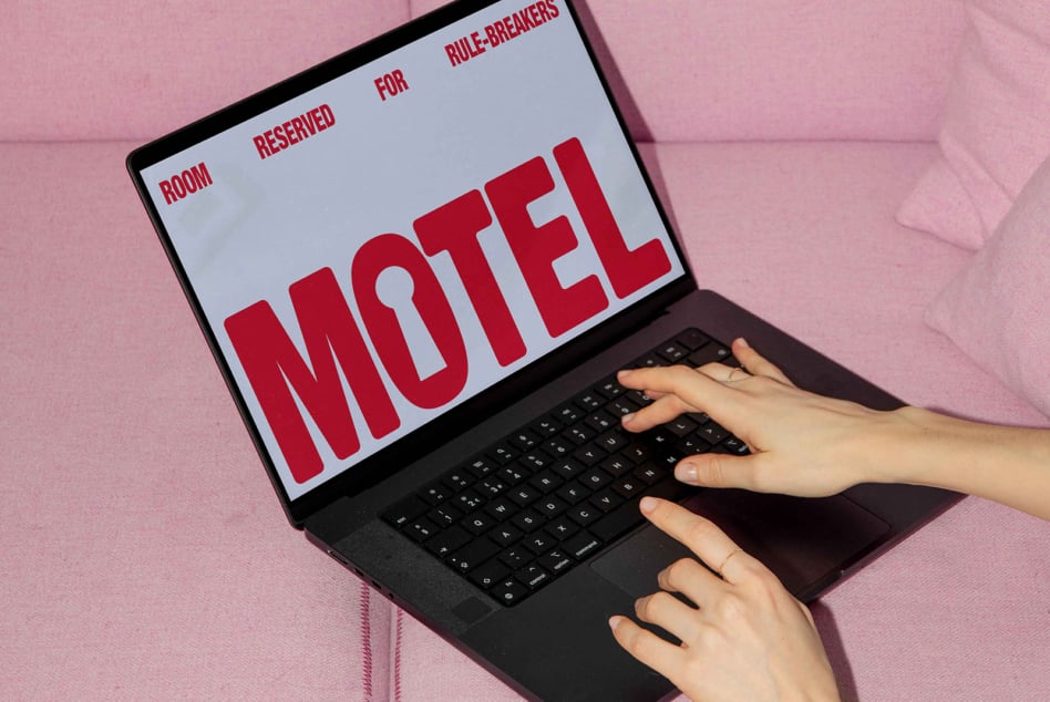 Laptop showing red motel sign with rule-breakers text on pink textured background