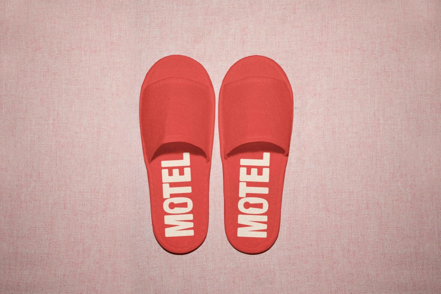 Red slippers with Motel text placed on a pink textured background ideal for graphics or mockups perfect for designers looking for eye-catching assets.