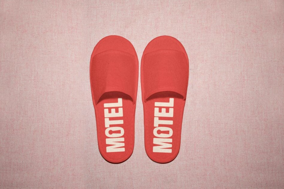 Red motel slippers with white lettering on dusty pink backdrop