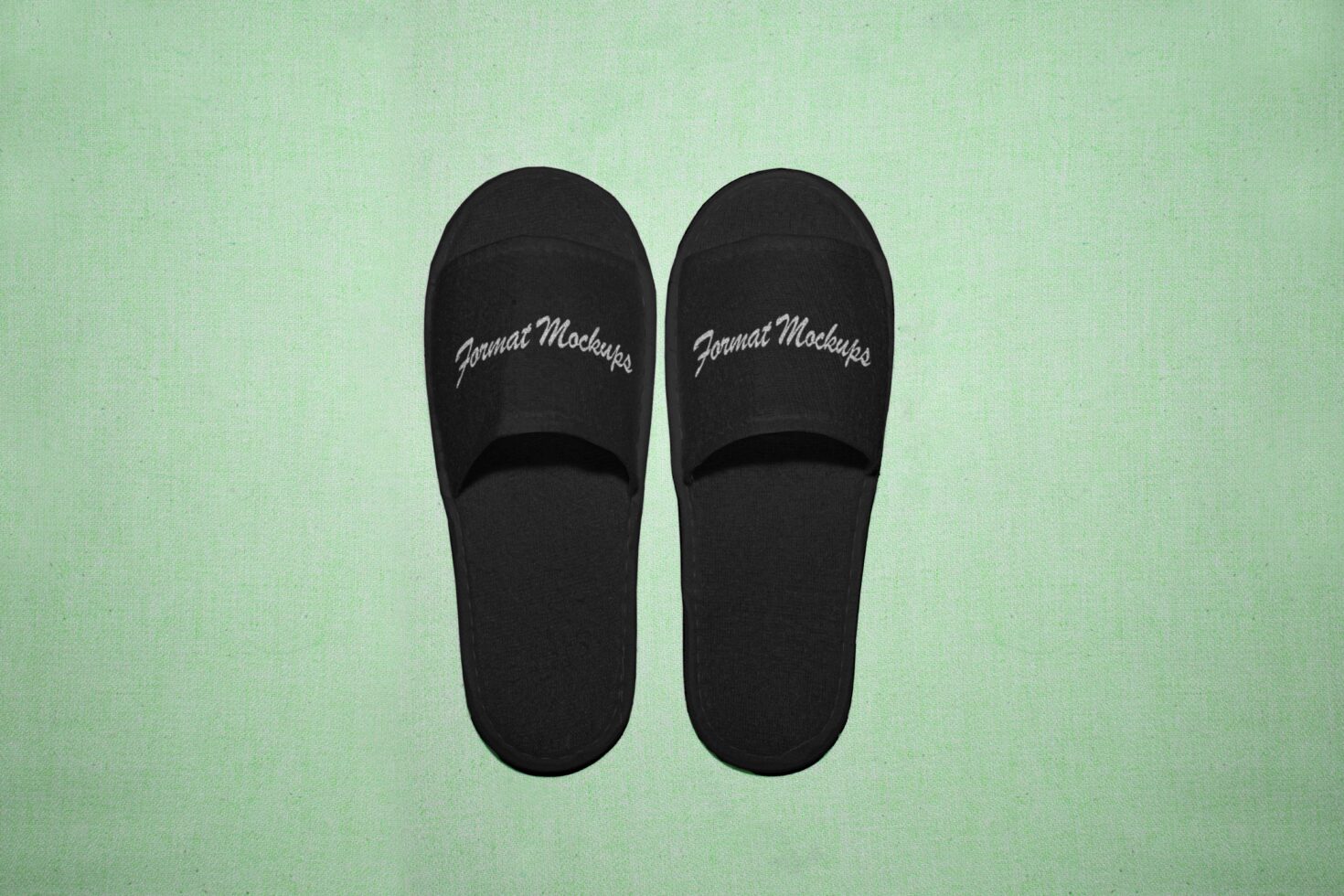 Black slipper mockup on a soft green fabric background ideal for footwear design projects customizable for branding or personal designs.