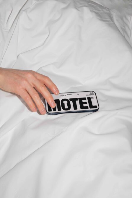 Hand holding motel key card mockup on white bedding background
