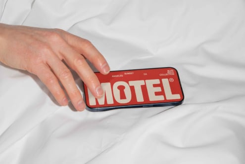 Hand holding smartphone on bed displaying Motel design with bold retro typography. Suitable for graphics or mockup templates. Ideal for designers.