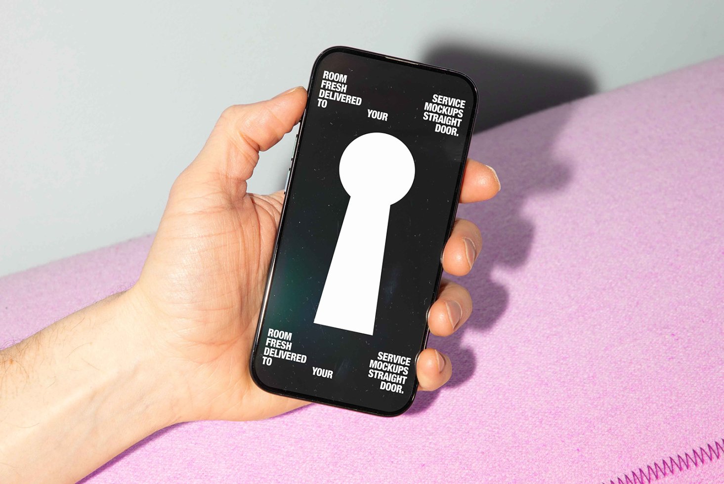 Mockup of a hand holding a smartphone with a keyhole graphic on screen. Text reads Room service fresh mockups delivered to your door. Design resources.