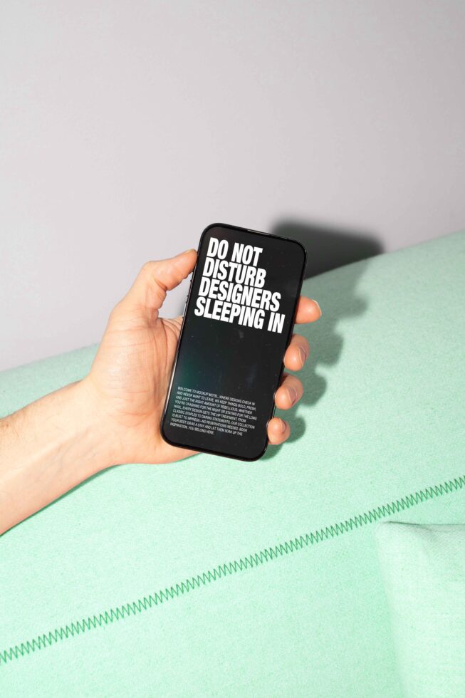 Designer holding smartphone with Do Not Disturb Designers Sleeping In text. Minimalist mockup for digital assets targeted at creative professionals.