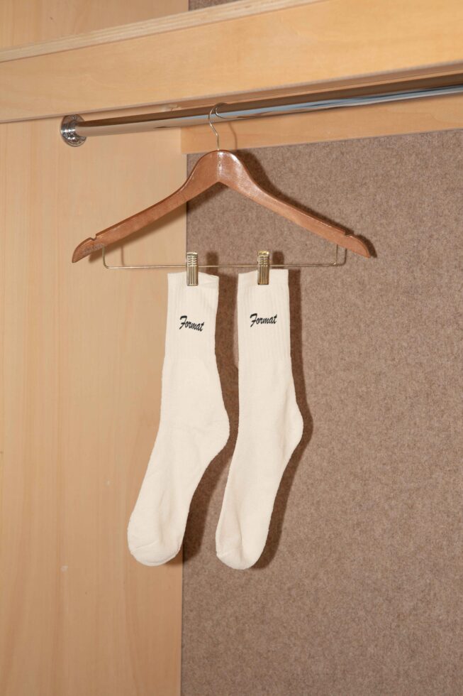 White socks with logo hanging on a wooden hanger in a closet setting perfect for apparel mockup or product design showcasing fashion templates