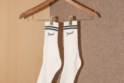 White socks with black stripes and logo hanging on a wooden hanger against a plain background. Suitable for apparel mockup, design projects, templates.
