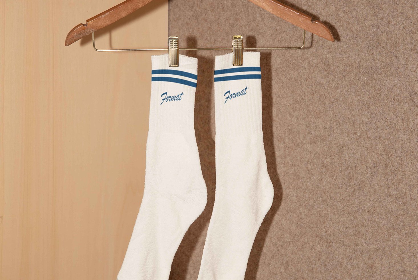 White socks with blue stripes and text hang on a wooden hanger against a neutral background Graphic design asset Mockup. Ideal for designers.