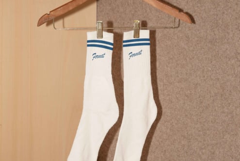 White socks with blue stripes and text hang on a wooden hanger against a neutral background Graphic design asset Mockup. Ideal for designers.