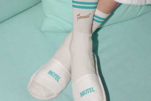Cozy mockup featuring white socks with blue stripes and slippers on a light teal sofa perfect for designers seeking stylish casual apparel graphics