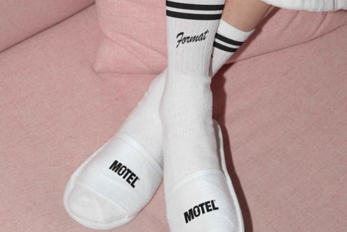 White socks with black stripes peeking out from under white slippers on pink fabric. Perfect for fashion mockups and apparel design showcases.