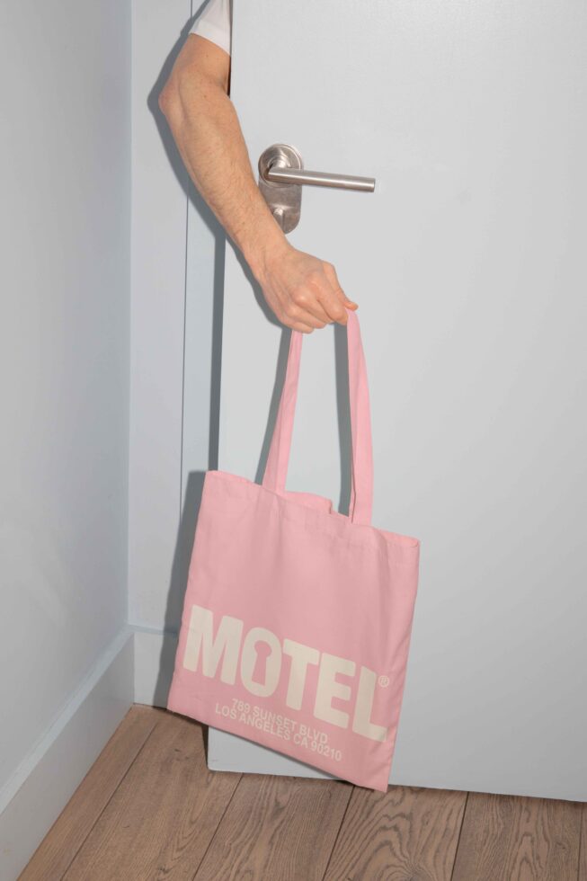 Man holds pink tote bag with MOTEL text, perfect for mockup design, branding projects, templates, typography, tote bag graphics, minimalist style