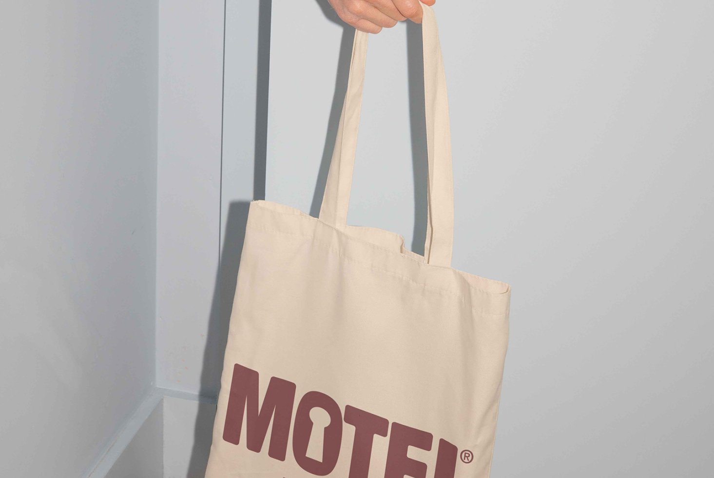Mockup of a beige tote bag with MOTEL text in bold maroon font, perfect for showcasing logo designs and branding. Ideal for graphic designers.