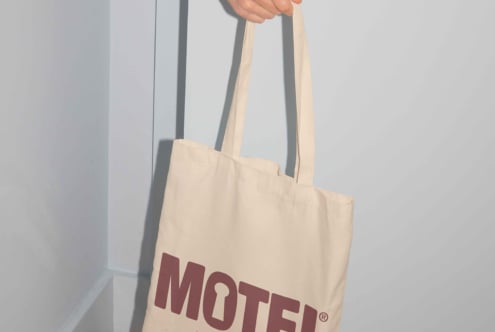 Mockup of a beige tote bag with MOTEL text in bold maroon font, perfect for showcasing logo designs and branding. Ideal for graphic designers.