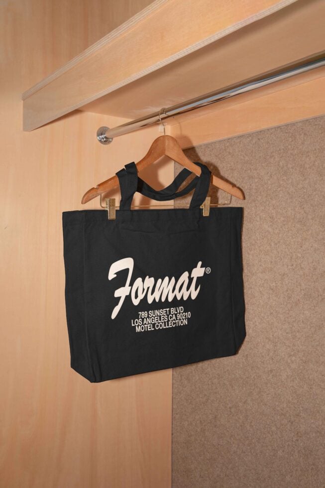 Black tote bag mockup hanging on a wooden hanger in a closet. Perfect for showcasing branding, logo design on bags. Ideal for graphic designers.