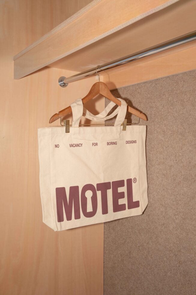 Tote bag with bold Motel logo in a minimalist closet, ideal for graphic design mockups and branding presentations for designers. Neutral toned setting.