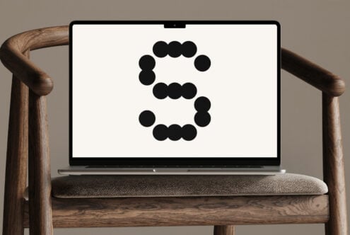 Laptop on wooden chair displaying large stylized letter S made of black dots against neutral background ideal for typography mockup or design assets