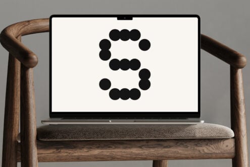 Laptop on wooden chair displaying a modern geometric dot font letter S, suitable for designers seeking creative typography, digital mockups, graphic design assets.
