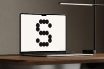Laptop showing abstract dotted letter S design on wooden desk with modern lamp. Ideal for mockup templates graphics and designer assets.