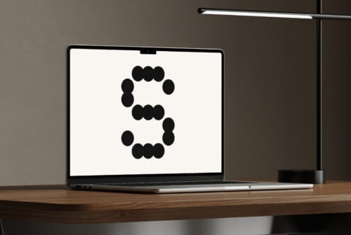 Laptop showing abstract dotted letter S design on wooden desk with modern lamp. Ideal for mockup templates graphics and designer assets.