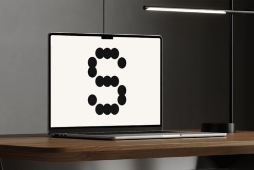 Laptop displaying a polka dot letter S against a white background on a wooden desk with modern lamp. Keywords: mockups, fonts, graphics, templates.