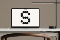 Laptop displaying modern typography design with stylized letter S in black dots minimalist workspace desk chair lamp graphic design mockup template