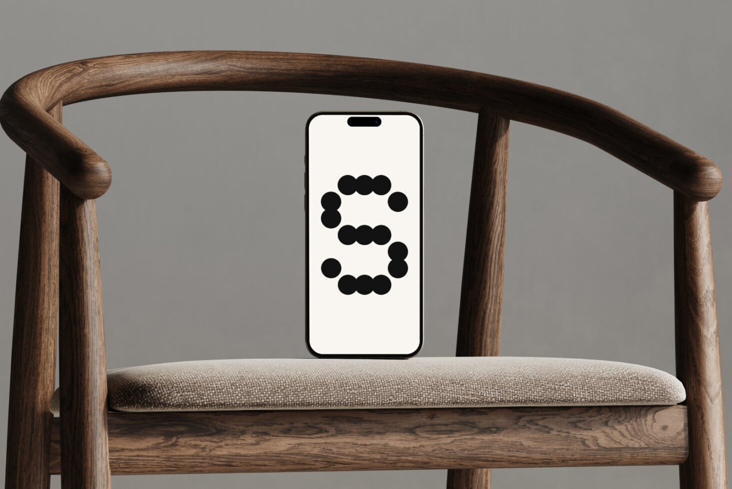 Modern smartphone mockup displaying a black dotted letter on screen, set against a stylish wooden chair backdrop. Ideal for graphic designers needs.