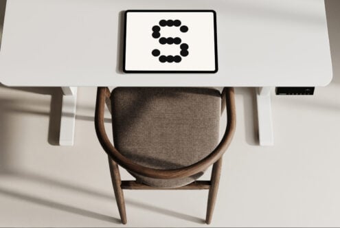 Stylish workspace mockup featuring tablet with letter S in a dot font on a white desk background. Ideal for branding and graphic design projects.