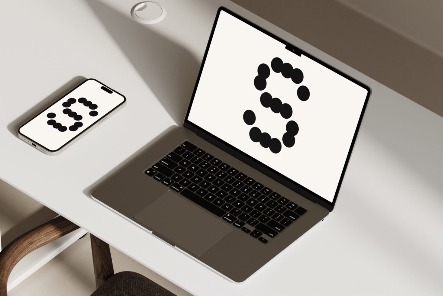 Mockup of a modern laptop and smartphone on a minimalist desk displaying a stylized letter S in a dot font. Perfect asset for graphic design templates.