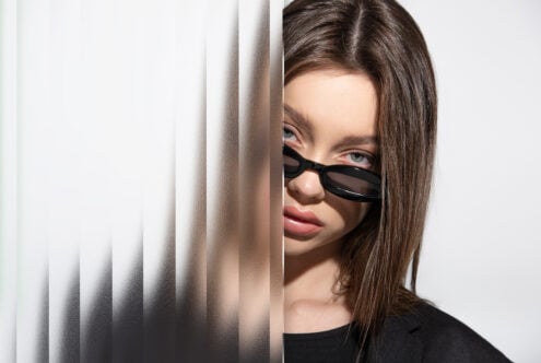 Woman with straight brown hair poses wearing sunglasses partially hidden behind a frosted glass panel fashion mockup minimalist designer asset