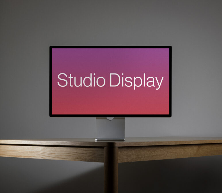 Horizontal desktop monitor on wooden desk showing pink gradient display