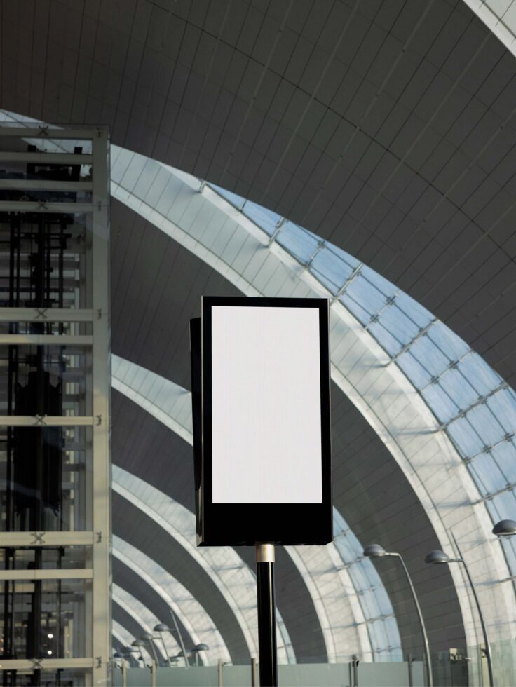 Mockup of a blank vertical signboard in a modern architectural space with curved roof and glass facade; ideal for digital asset designers and graphics projects.