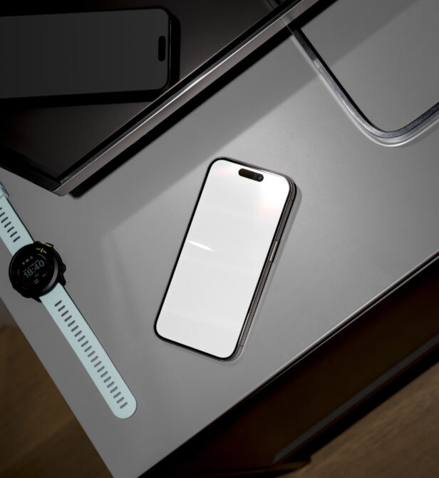 Overhead flat lay of phone, smartwatch, tablet, laptop arranged on gray desk surface