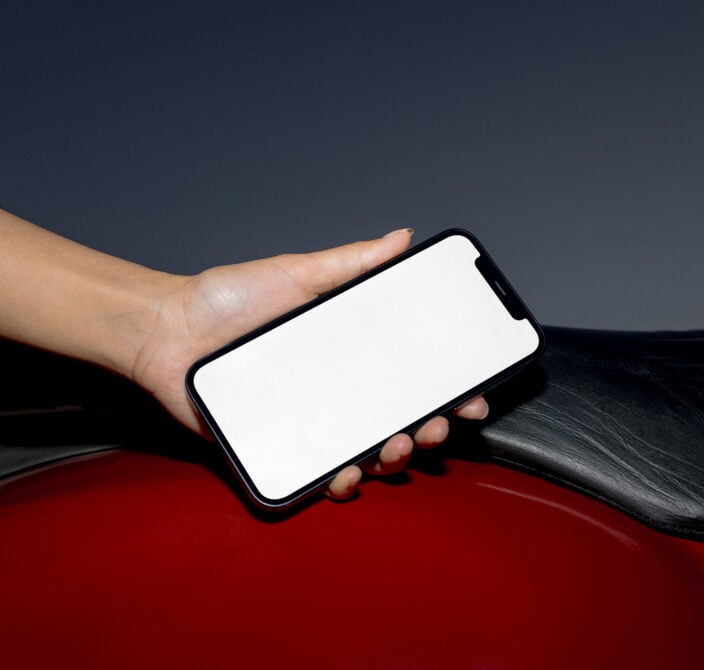 Hand holding black phone with blank screen against red surface