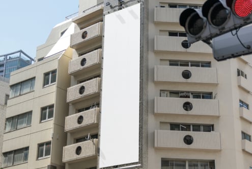 Blank vertical billboard on urban building facade ideal for advertising mockup. Cityscape background with modern architecture. Perfect for designers.
