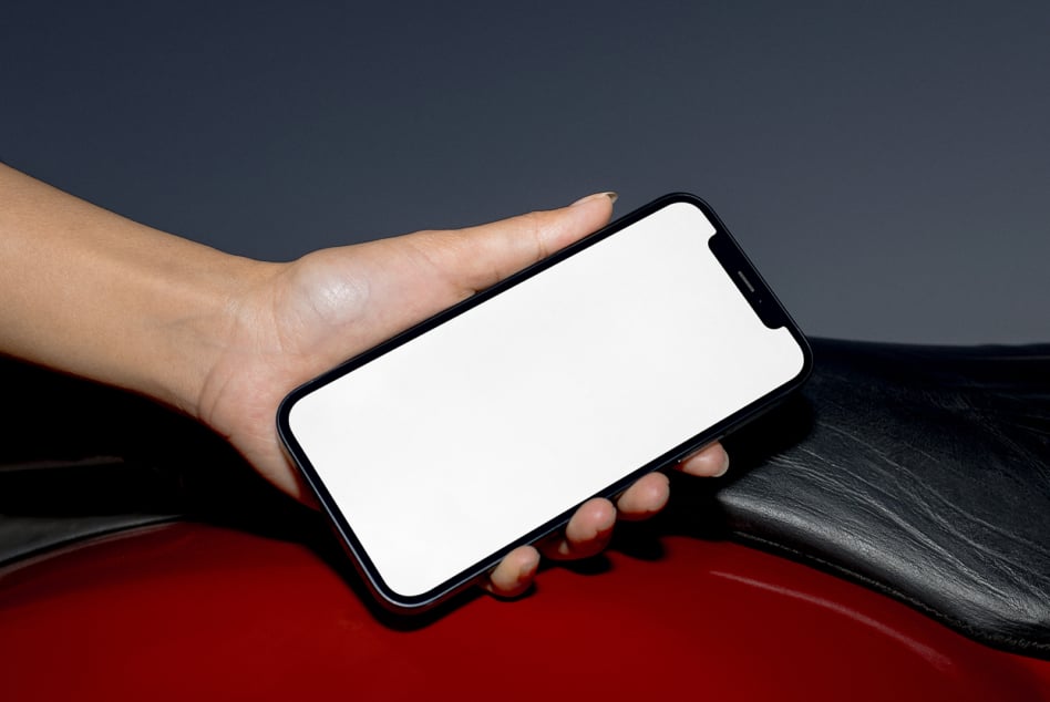 Hand holding black phone with blank screen over red leather background