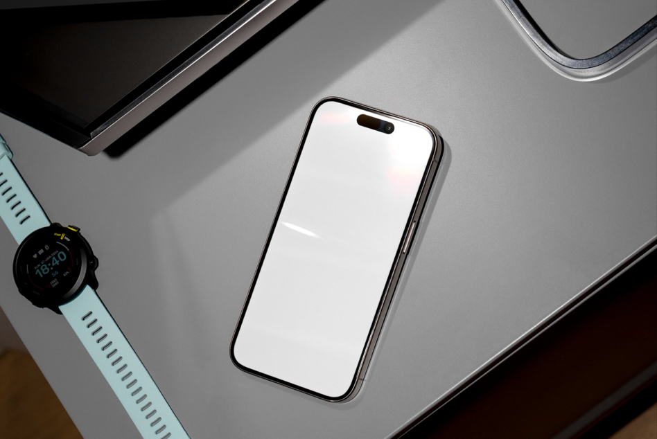 Black smartphone with blank white screen on gray desk with watch
