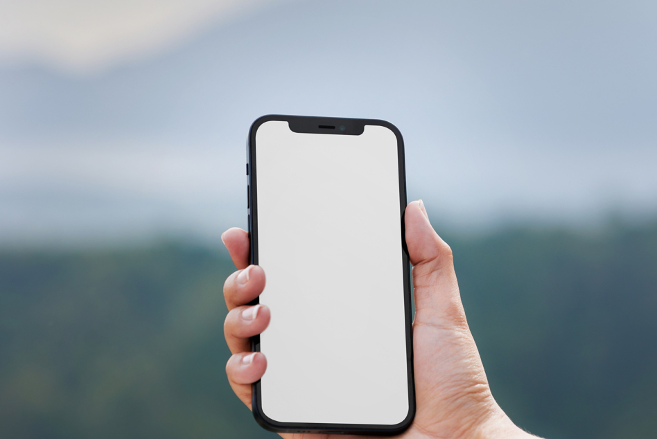 Hand holding iPhone with blank white screen against blurred outdoor landscape background