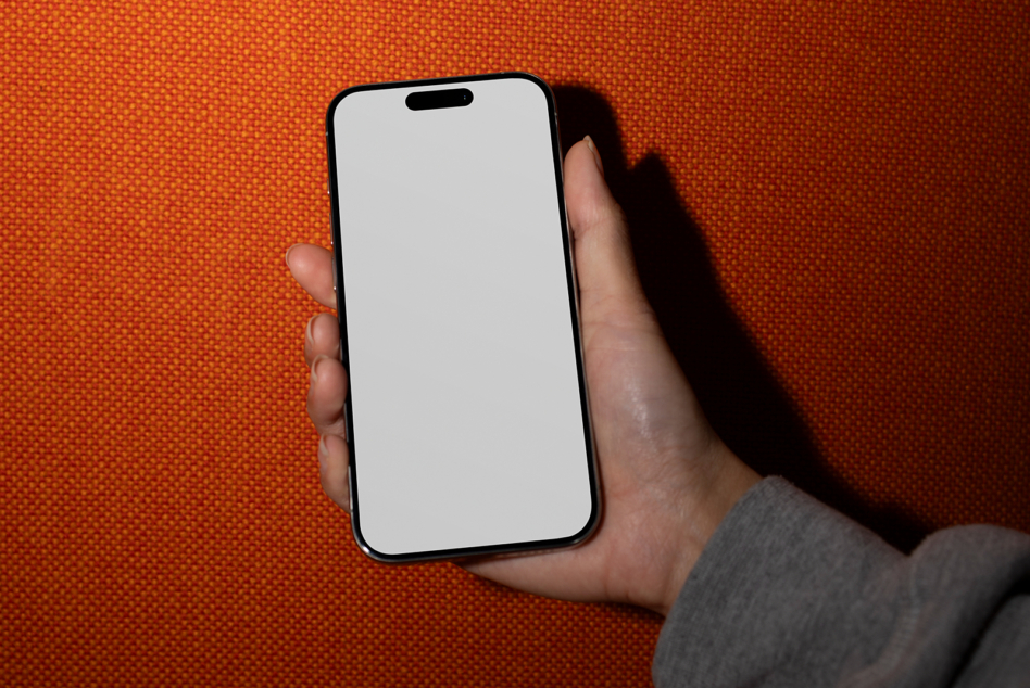 Hand displaying black phone with white blank screen, orange background