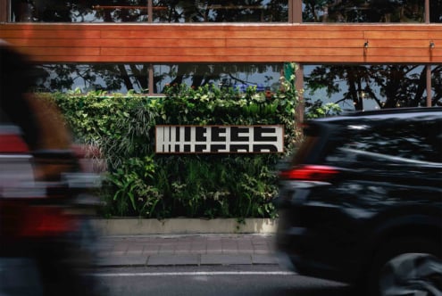 Street view with cars blurred in motion, modern signage on green wall, wooden facade, urban environment, graphic design inspiration, architecture, mockup.