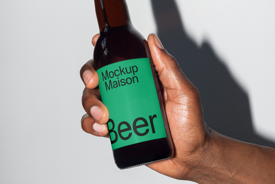 Hand holding dark beer bottle with green label displaying Mockup Maison design