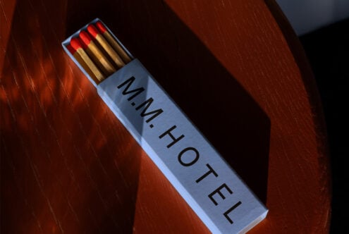Matchbox on wooden surface labeled MM HOTEL featuring red-tipped matches. Perfect for branding mockups or graphic design templates. High-quality asset.