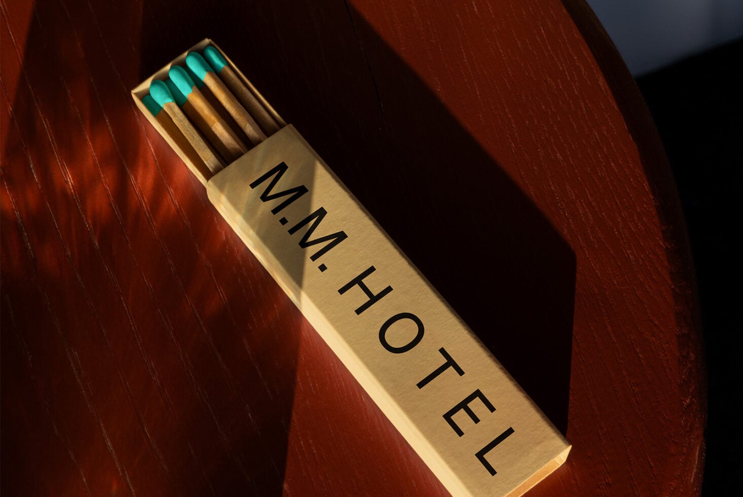 Cream colored matchbox with teal match tips resting on rich mahogany wood