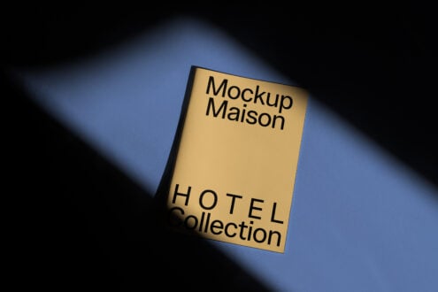 Yellow booklet on a blue surface with elegant shadows reads Mockup Maison Hotel Collection. Perfect for design templates and mockup demonstrations.